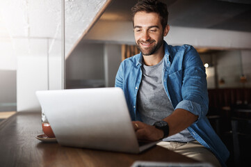 Free wifi with compliments of the cafe. a handsome young man using a laptop in a coffee shop.