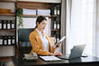 © laddawan - Young beautiful woman typing on tablet and laptop while sitting at the working wooden table office.