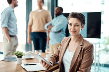 Making solid progress with the right tools. Portrait of a young businesswoman using a digital tablet with her colleagues in the background.