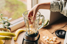 Woman is preparing a healthy detox drink in a blender - a green smoothie with fresh fruits, green spinach and avocado. Healthy eating concept, ingredients for smoothies on the table, top view