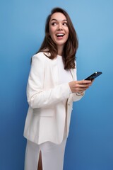 Wall Mural - a woman with dark long hair in an elegant white dress holds a smartphone and chats on the Internet