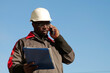 © Harmony Video Pro - African american builder with work papers talks on smartphone