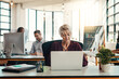 © Nola V/peopleimages.com - You wont find a more productive workspace. a mature businesswoman using a laptop in a modern office with her colleagues in the background.