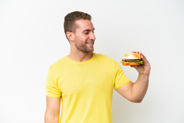 Canvas Print - Young caucasian man holding a burger isolated on white background with happy expression