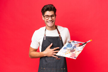 Wall Mural - Young artist caucasian man holding a palette isolated on red background smiling a lot