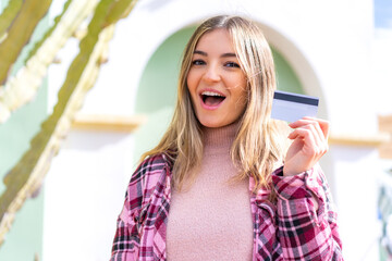 Wall Mural - Young pretty Romanian woman holding a credit card at outdoors with surprise and shocked facial expression