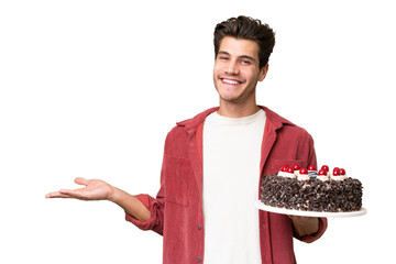 Wall Mural - Young caucasian man holding birthday cake over isolated background extending hands to the side for inviting to come