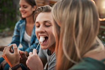 Leinwandbilder - Open wide. a young cheerful man being fed a marshmallow by his girlfriend while being seated outside.