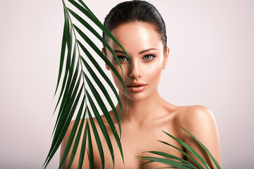 Young beautiful woman with green leaves near face and body. Skin care beauty treatments concept.  Closeup girl's face with green leave. White model with clean, health skin of face - posing at studio