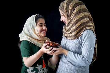 Wall Mural - Beautiful Asian Muslim woman with daughter girl wear hijab scarf and traditional costume, hold date fruits together, sweet and energy boost food mostly eat in Ramadan of Islam on dark black background