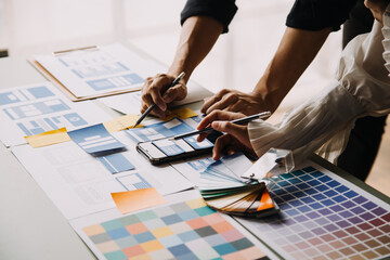 Close up ux developer and ui designer brainstorming about mobile app interface wireframe design on table with customer breif and color code at modern office.Creative digital development agency