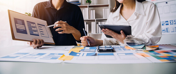 Close up ux developer and ui designer brainstorming about mobile app interface wireframe design on table with customer breif and color code at modern office.Creative digital development agency