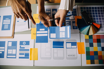 Close up ux developer and ui designer brainstorming about mobile app interface wireframe design on table with customer breif and color code at modern office.Creative digital development agency