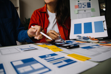 Close up ux developer and ui designer brainstorming about mobile app interface wireframe design on table with customer breif and color code at modern office.Creative digital development agency