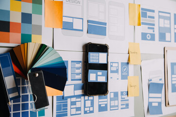 Close up ux developer and ui designer brainstorming about mobile app interface wireframe design on table with customer breif and color code at modern office.Creative digital development agency