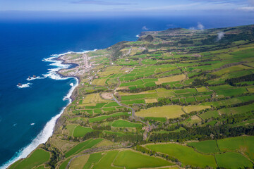 Wall Mural - Aerial view of the coastline on Sao Miguel Island, with town buildings, green farmland and volcanic mountains, Azores, Portugal