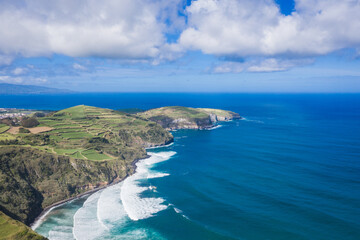 Wall Mural - Aerial view of the coastline on Sao Miguel Island, with town buildings, green farmland and volcanic mountains, Azores, Portugal