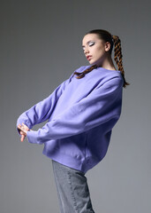 Canvas Print - a fashionable woman in a lilac sweatshirt poses on a gray background