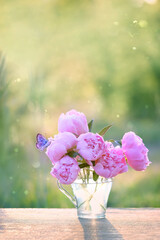 Wall Mural - butterfly and pink peony flowers in glass cup on table in garden, abstract natural background. gentle romantic composition with flowers. spring, summer season. template for design. copy space