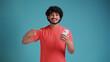 © Виталий Лысак - Jubilant exultant happy young bearded latin or arabian man 20s years old hold in hand use mobile cell phone pointing on smartphone, in coral t-shirt on blue studio background