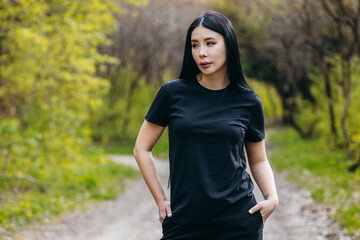 Wall Mural - Stylish brunette asian girl wearing black t-shirt posing against nature