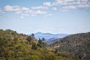 two mountains forming a V and in the center another mountain further away with cooler tones under a blue sky with white clouds