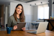 © Dorde - Smiling confident businesswoman looking at camera sitting at home office desk. Modern stylish female corporate employee successful executive manager holding digital tablet posing for business portrait