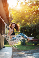 happy young female riding on macrame swing chair near country house outdoors