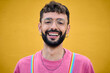 © CarlosBarquero - Close up smiling cheerful young Caucasian man holding his rainbow lgbt suspenders. Gay people posing for photo yellow background. Cheerful gay bearded person happy studio photo isolated. Millennials.