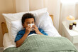 © New Africa - African-American boy with scarf and tissue blowing nose in bed indoors, above view. Cold symptoms