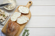 Slices of baguette with tofu cream cheese and rosemary on white wooden table, flat lay. Space for text