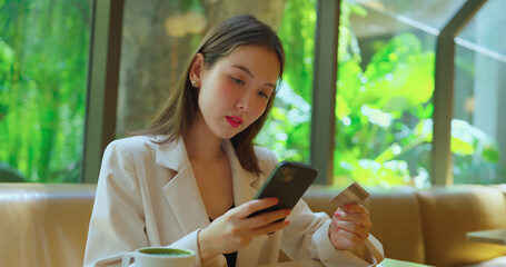 Woman holding credit card and smartphone in hand. She using credit to shopping online in restaurant.