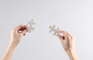 Wall Mural - Woman's hands hold puzzle pieces on gray background. Business concept, teamwork