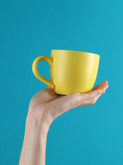 Wall Mural - Woman's hand holds a yellow ceramic cup on a blue background