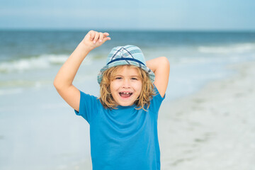 Summer vacation concept. Happy little kid walking on sea sandy beach. Travel and adventure kids concept. Lovely kid play outdoor. Pretty little child in hat relaxing on the beach near sea, summer