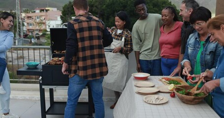 Wall Mural - Multiracial friends having fun  while preparing food during weekend day - Multi generational people doing barbecue at home's rooftop - Asian woman cooking meat on bbq grill