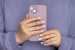 © Evgeniya Grande - Close-up woman with white wanicure hold in hand and use mobile cell phone in puple case with ring. No face.