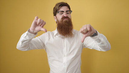 Canvas Print - Young redhead man doing negative gesture with thumbs down over isolated yellow background