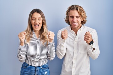 Poster - Young couple standing over blue background excited for success with arms raised and eyes closed celebrating victory smiling. winner concept.