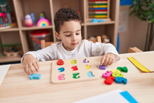 Adorable Hispanic Boy Playing With Maths Puzzle Game Sitting On Table At Kindergarten