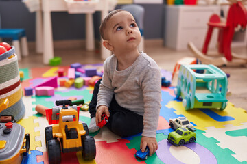 Adorable hispanic boy playing with car toy sitting on floor at kindergarten