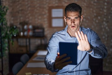 Wall Mural - Handsome hispanic man working at the office at night doing stop gesture with hands palms, angry and frustration expression