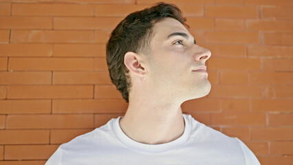 Young hispanic man looking to the side with serious expression over isolated brick background