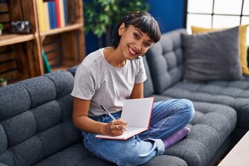 Young woman writing on book sitting on sofa at home