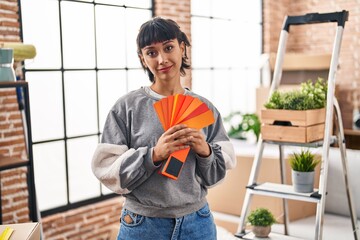 Wall Mural - Young hispanic woman moving to a new home choosing paint relaxed with serious expression on face. simple and natural looking at the camera.