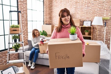 Poster - Mother and daughter moving to a new home holding cardboard box clueless and confused expression. doubt concept.