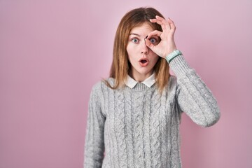 Canvas Print - Beautiful woman standing over pink background doing ok gesture shocked with surprised face, eye looking through fingers. unbelieving expression.