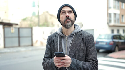 Wall Mural - Young bald man using smartphone with serious expression at street