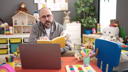 Canvas Print - Young bald man preschool teacher reading story book on a video call at kindergarten