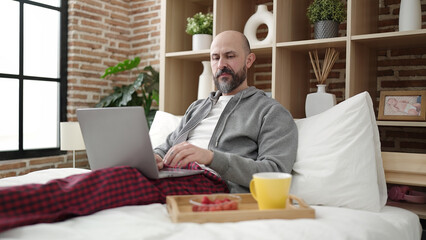 Wall Mural - Young bald man having breakfast using laptop at bedroom